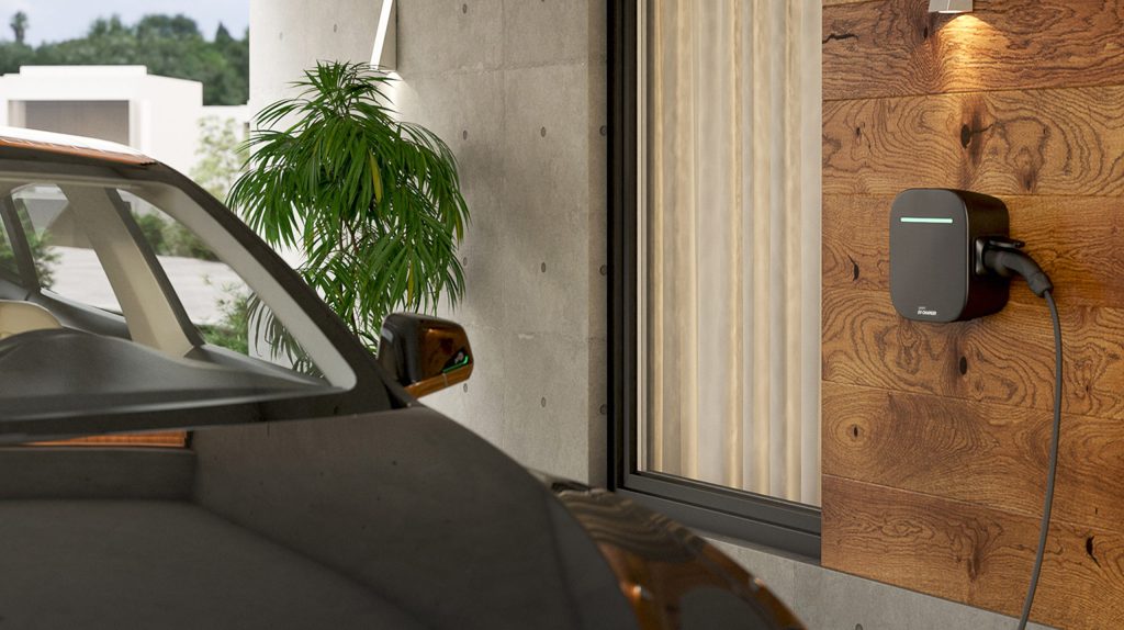 A sleek black EV wall charger with a glowing green light strip is mounted on a wooden-paneled wall, with its cable plugged into a dark-colored electric vehicle partially visible in the foreground.
