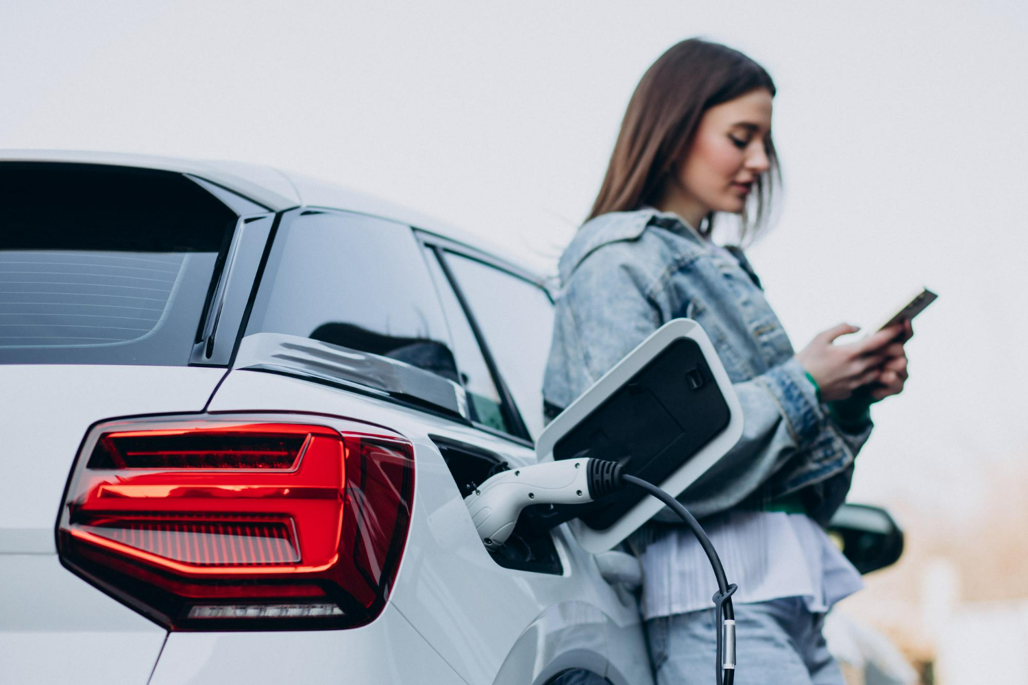 Woman using her smartphone while her electric vehicle charges via an OCPP-enabled charger, highlighting seamless connectivity and smart charging management.