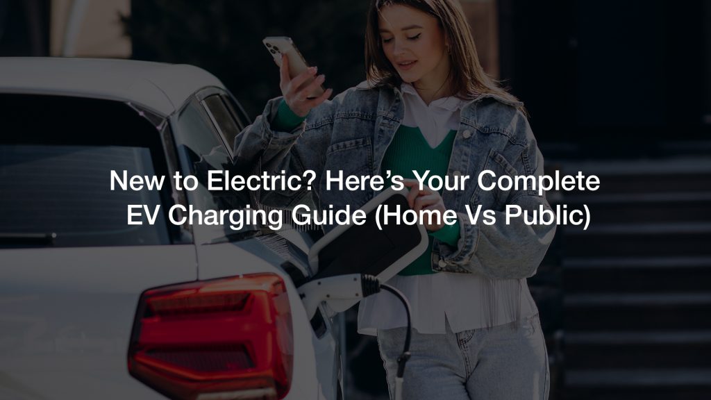 The image shows a person, from the chest down, wearing a denim jacket over a green sweater and light-colored jeans, holding a white EV charging cable and preparing to plug it into the charging port of a white electric vehicle.